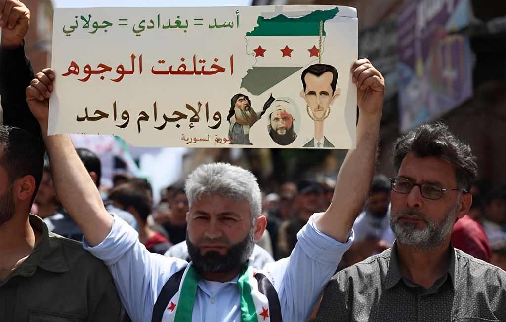 A protester at an anti-Hayat Tahrir al-Sham rally in Binnish, Idlib province, May 17, 2024. The sign reads: “Assad = Baghdadi = al-Jolani. Different faces, same crime.”